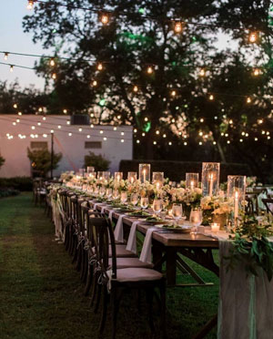 Outdoor reception with many candles on a long table and string lights overhead